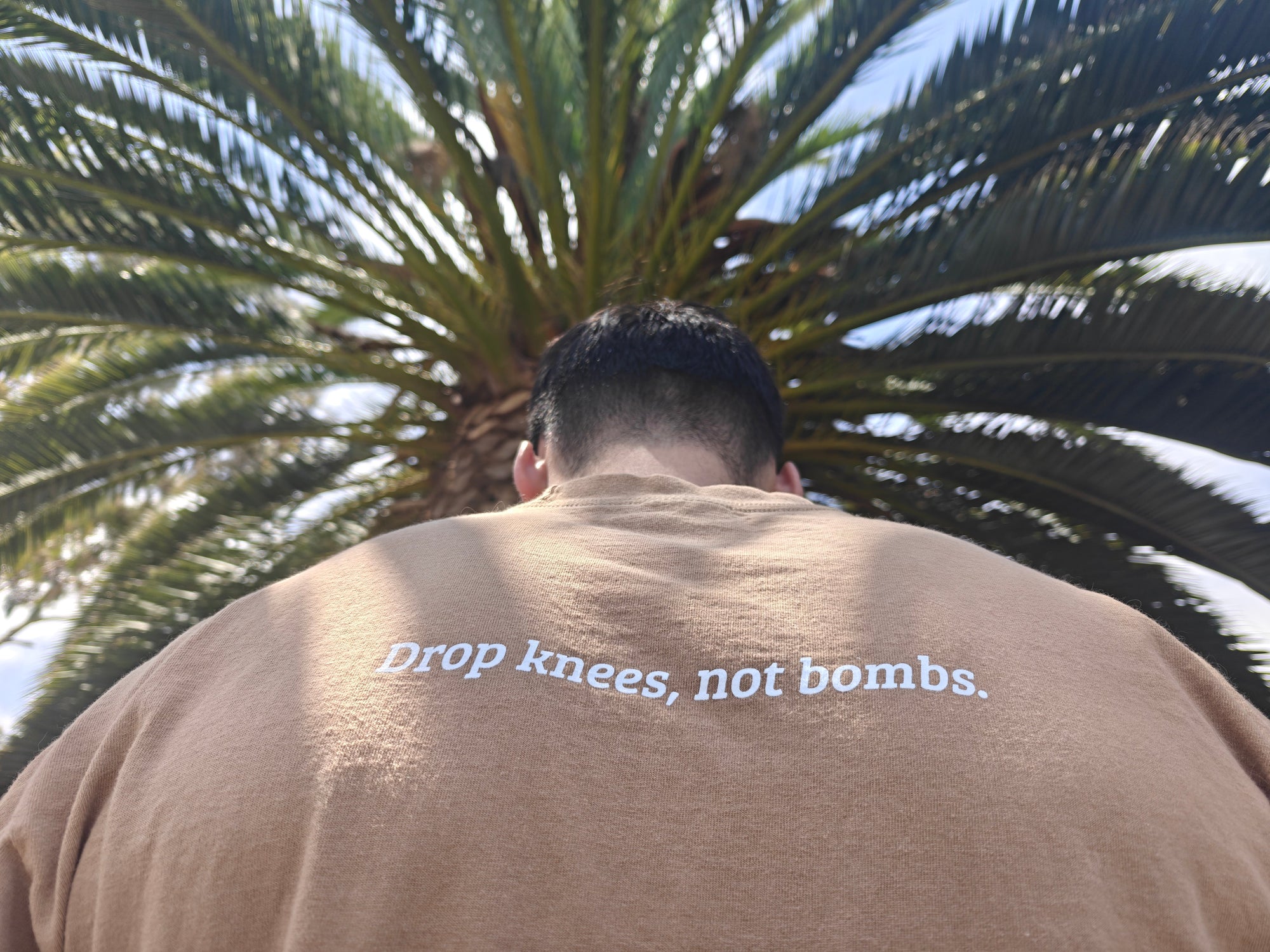 Sand tee - back with Drop Knees Not Bombs text